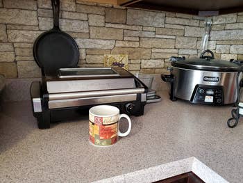 A reviewer's grill closed on a counter with a coffee mug in front to show how small it is