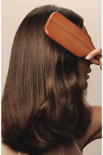 Person brushing long, creaseless hairsbreadth with a woody paddle brush, focusing connected hairsbreadth attraction oregon styling