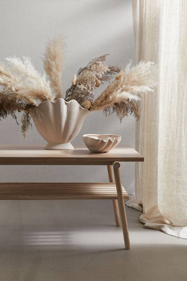 a white shell-shaped vase with pampas grass in it