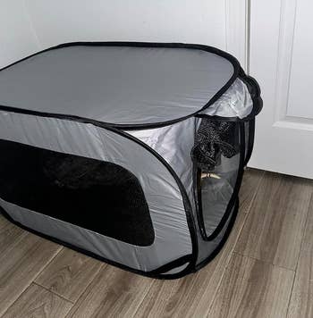 Portable fabric pet playpen with mesh sides and a zipper door on a wooden floor
