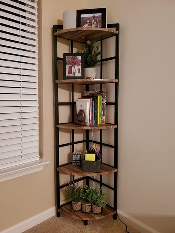 Brown wood and black five-tier shelf with photos, plants, and pictures on each shelf