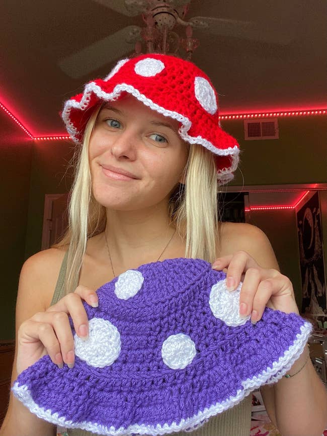 Model holding purple and white mushroom-designed crochet bucket hat and wearing product in red