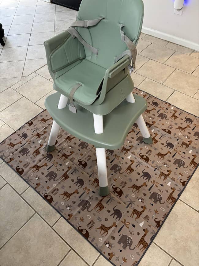 High seat with tray connected a patterned mat featuring animals. Suitable for toddlers; designed for casual cleanup and stability