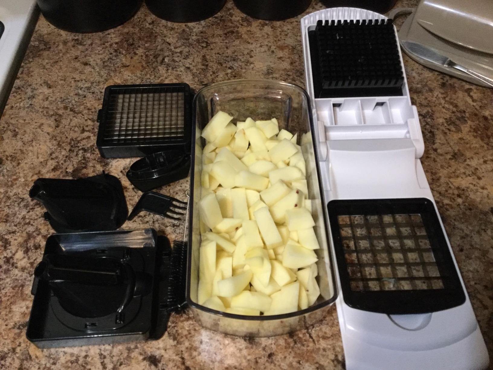 a reviewer photo of the chopper, attachable blades and a bin filled with chopped potatoes  