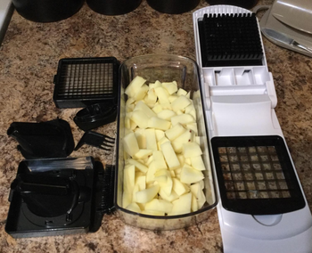 a reviewer photo of the chopper, attachable blades and a bin filled with chopped potatoes  