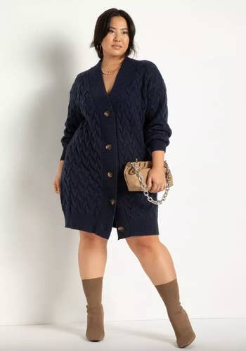 model wearing the cardigan dress in navy blue, holding clutch purse