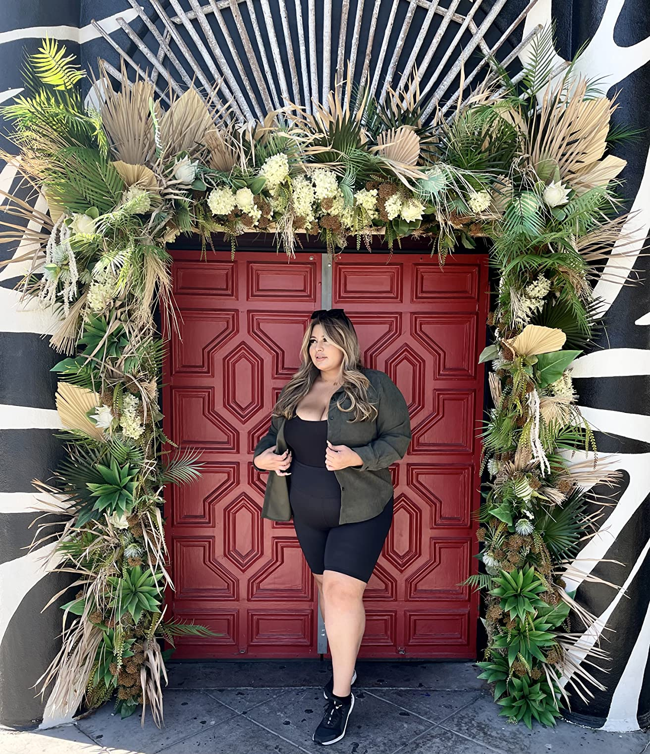 Person successful  casual attire, wearing a achromatic  formal  and greenish  jacket, stands by a decorated doorway with greenery and pampas grass, suitable for buying  content