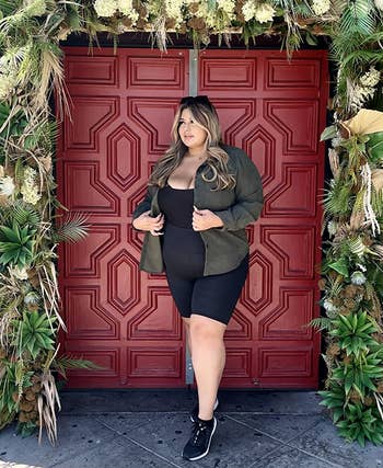 Person successful casual attire, wearing a achromatic formal and greenish jacket, stands by a decorated doorway with greenery and pampas grass, suitable for buying content