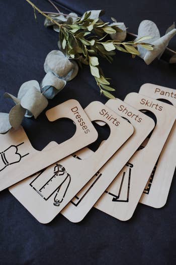 Wooden closet dividers labeled Dresses, Shirts, Shorts, Skirts, and Pants laid retired  connected  a table