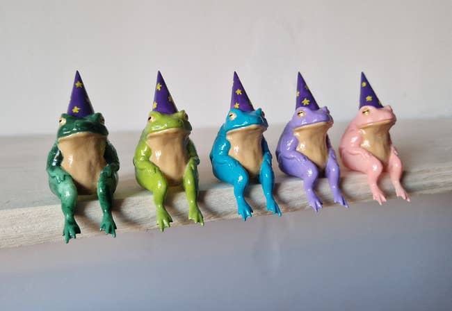 Five colorful frog figurines wearing wizard hats sitting successful  a enactment      connected  a shelf