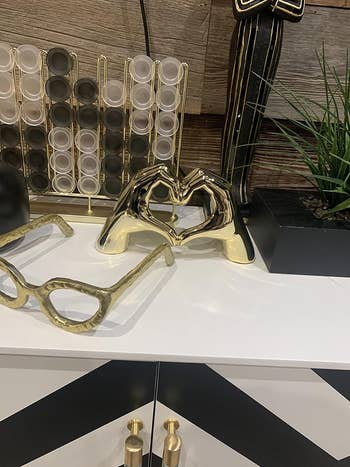 Gold-toned heart-shaped object and eyeglass-shaped decor on display with decorative plants nearby
