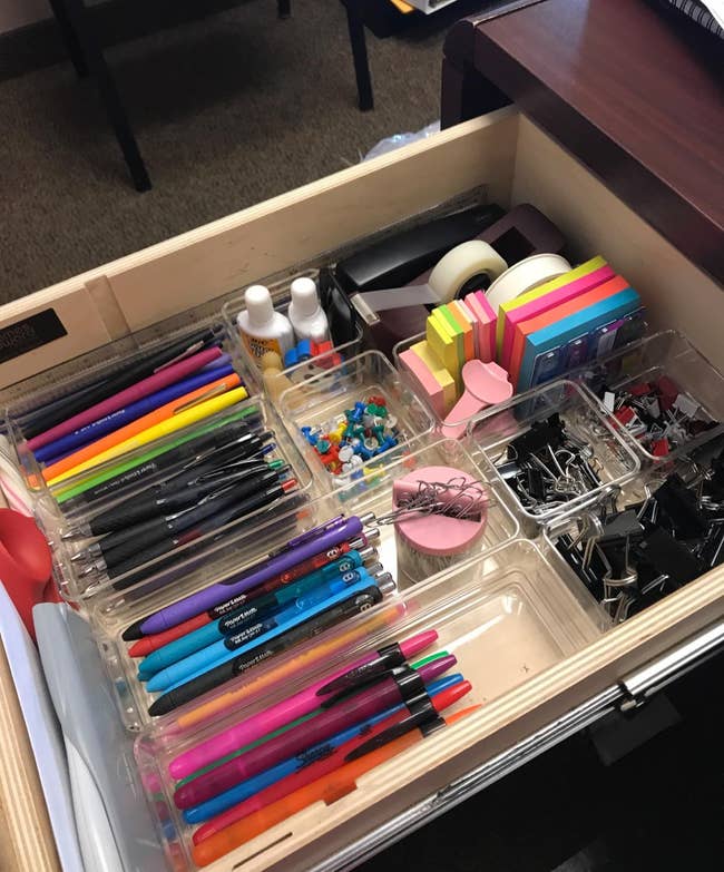 desk drawer with a variety of clear bins inside organizing various small office items