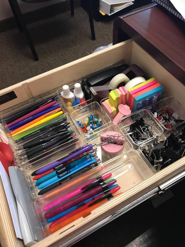 desk drawer with a variety of clear bins inside organizing various small office items