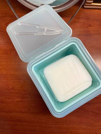 Clear storage container on a wooden surface with a white folded towel inside
