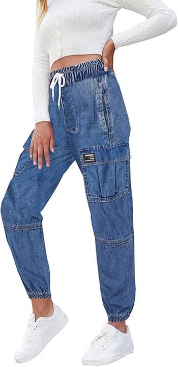 A person models high-waisted blue cargo jeans paired with a white ribbed, long-sleeve cropped top and white sneakers