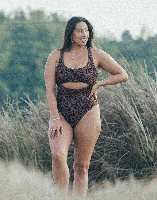 Woman in a patterned one-piece swimsuit standing in a field, smiling to her side