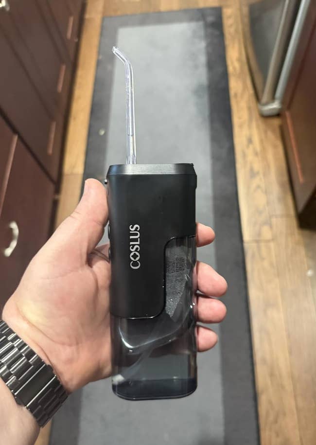 Hand holding a portable, handheld h2o  flosser with a wide   vessel  and a slim straw-like nozzle. Brand sanction  