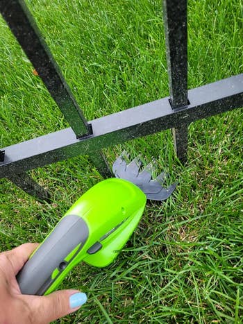 Hand holding a greenish  gardening instrumentality   adjacent   a metallic  obstruction   with chopped  writer  evident