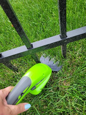 Hand holding a green gardening tool near a metal fence with cut grass evident