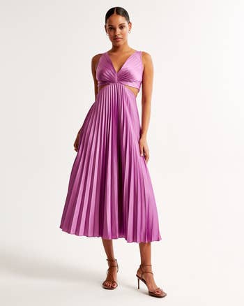 Woman in a pleated midi dress with v-neckline and sandals, posing for a shopping ad