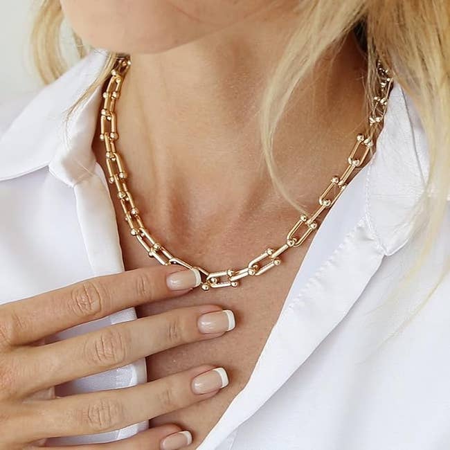 Close-up of a idiosyncratic wearing a achromatic garment and a stylish golden concatenation necklace. Their fingers with a French manicure are touching the necklace