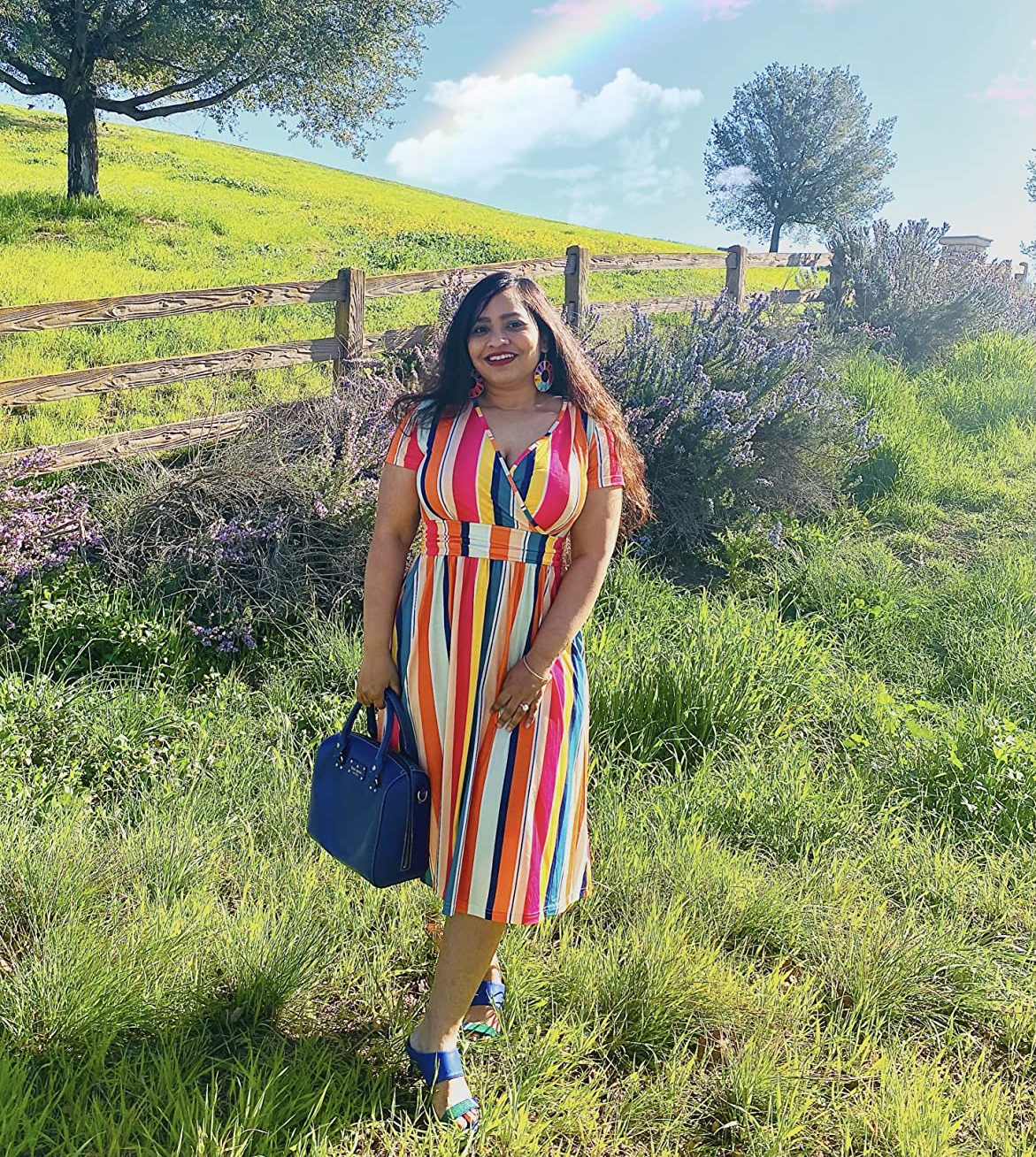 Reviewer is wearing the multi-colored vertically striped wrap dress with blue shoes and a blue bag