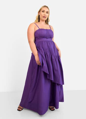 Model wearing a sleeveless, floor-length purple formal  with layered skirt, posing confidently successful  a shopping-related setting