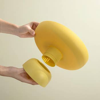 Hands assembling a modern yellow lamp with a round base, showcasing its detachable parts