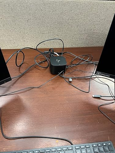 Messy desk with tangled cables connected to a small electronic device between two monitors and a keyboard