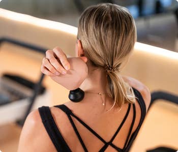 Woman in activewear using a compact massage device on her shoulder