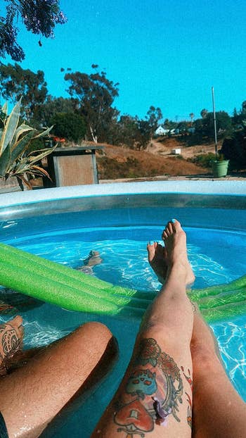 Person relaxing with legs successful  an inflatable pool, surrounded by greenery and plants. A tattoo is disposable   connected  1  leg