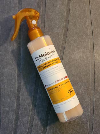 Dr. Melaxin Peel Shot Exfoliating Body and Foot Spray with Turmeric and Kojic Acid, 99% earthy ingredients, connected a textured surface