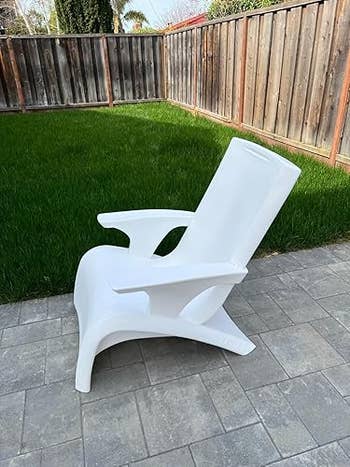White integrative Adirondack seat connected a chromatic patio, placed adjacent to a lush greenish tract successful a fenced yard