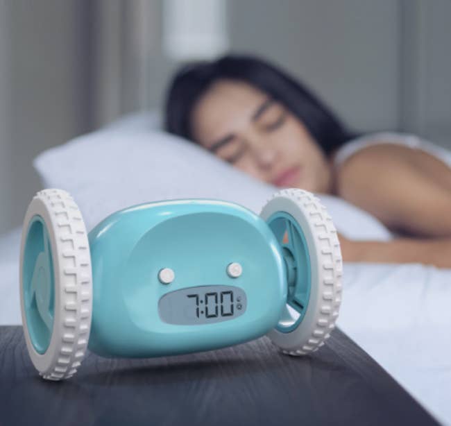 Wheel-shaped alarm clock on a table with a sleeping woman in the background