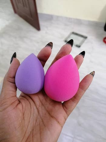 Hand holding two makeup sponges, one purple and one pink