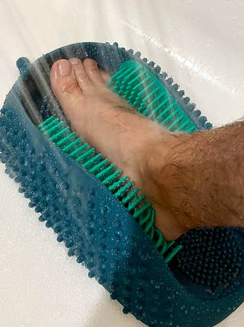 Person using a foot scrubber mat in the shower for sole cleaning and massage