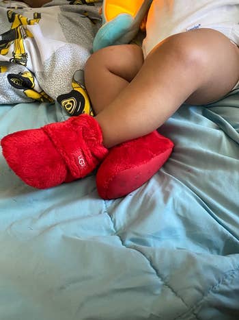 a reviewer photo of a baby wearing the uggs in red