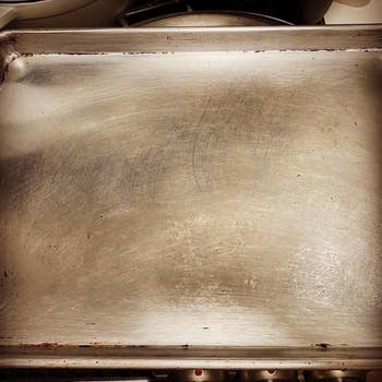 Close-up of a well-used baking sheet with scratches and slight discoloration, suggesting frequent use and durability in cooking