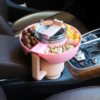 Snack tray and drink container with straw on a car's console, holding popcorn, chocolate balls, and sunflower seeds