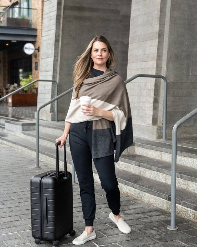 The model wrapped in the scarf standing next to a suitcase with a cup of coffee in hand 