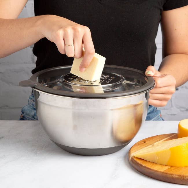 a model shredding cheese into a stainless steel mixing bowl