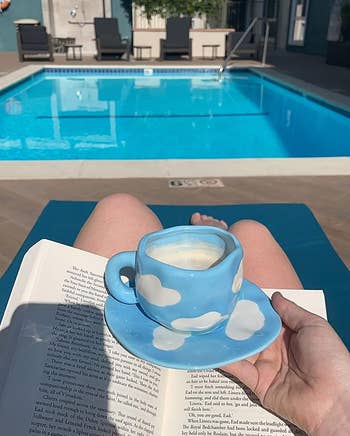 a reviewer using an irregular coffee mug that is light blue with white clouds on it 