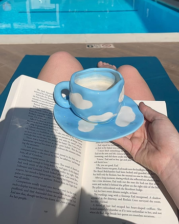 a reviewer using an irregular coffee mug that is light blue with white clouds on it 