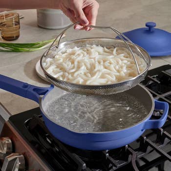 hand pulling noodles in strainer basket out of bright blue pan