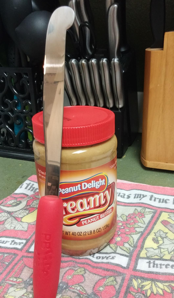 reviewer photo of the peanut butter knife leaning against a jar of peanut butter to show scale
