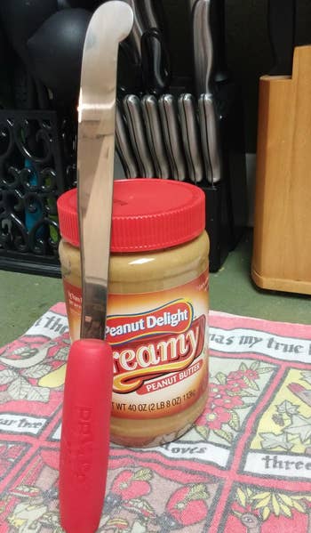 reviewer photo of the peanut butter knife leaning against a jar of peanut butter to show scale