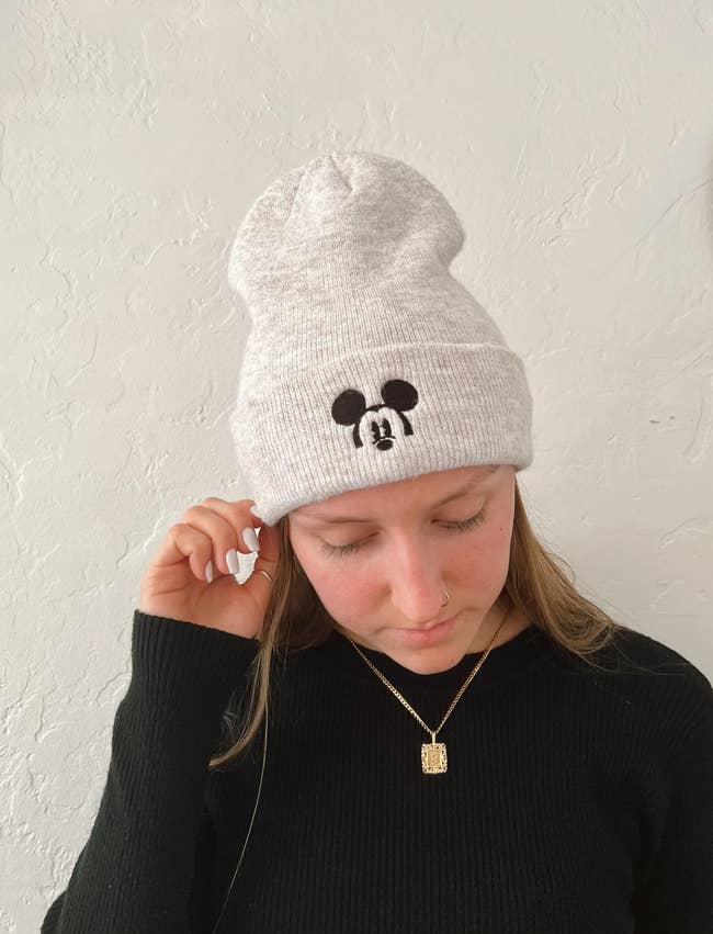 a model in an oatmeal colored beanie with mickey patch on it