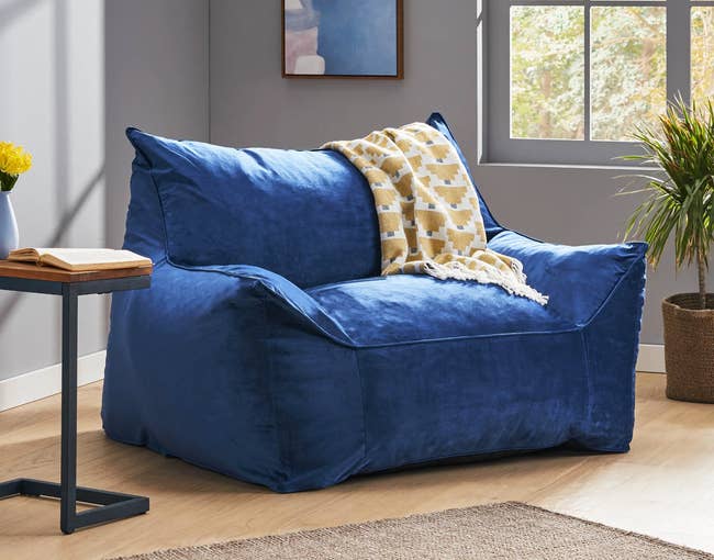 Cobalt blue large plush bean bag chair with armrests on a hardwood floor and yellow throw blanket