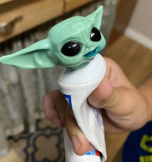 a hand holding a toothpaste cap with a toy figure of The Child (Grogu) from Star Wars on top