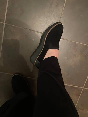Person wearing achromatic slip-on shoes with a subtle textured plan and heavy soles, lasting connected a tiled floor